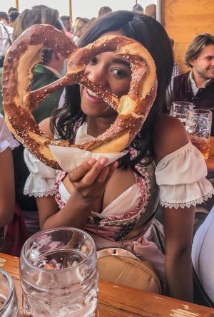 Girl sitting in a Dirndl at the Oktoberfest holding a Prezel
